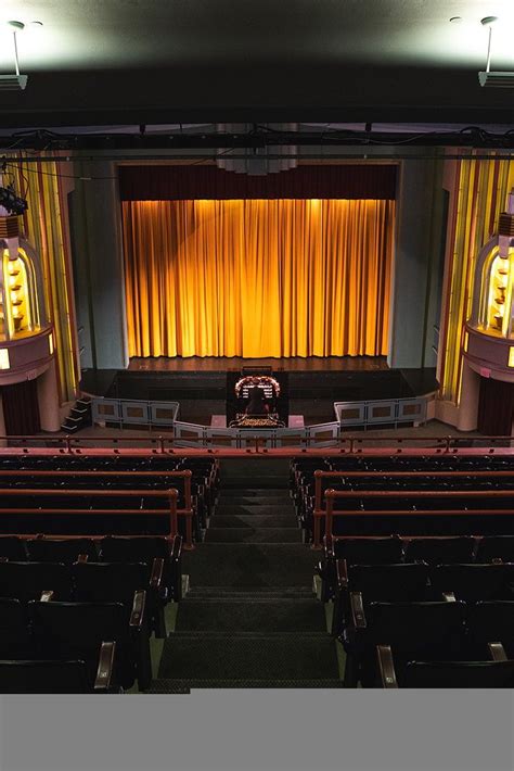 an empty auditorium with yellow drapes and black seats in front of the ...