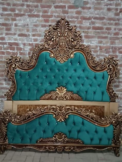 an ornate gold and turquoise bed frame against a brick wall with white bricks in the background