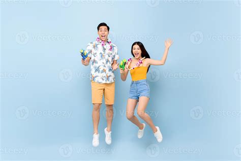 Young Asian couple in summer outfits with water guns jumping in studio blue background for ...