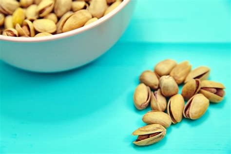 Premium Photo | Pistachio nuts in pink bowl on blue wooden table background