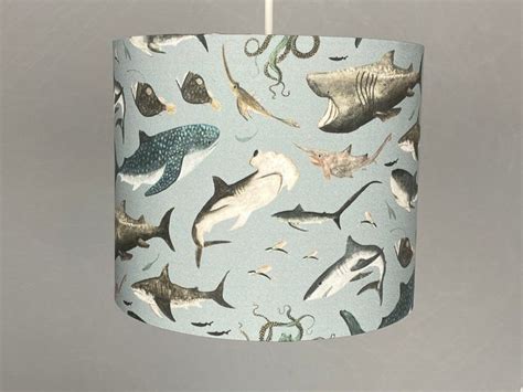 a blue lamp shade with sharks and sea creatures on it, hanging from a white cord