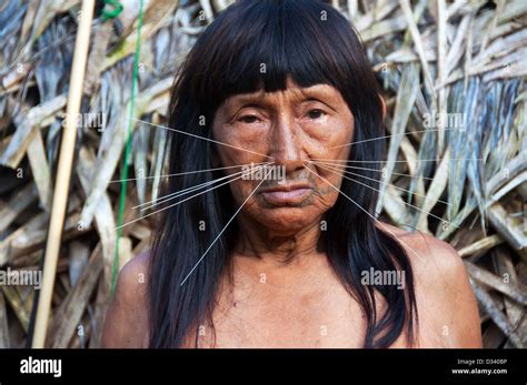 A Matses Mayorunas elderly woman with traditional whiskers and tattoos in front of a maloca ...