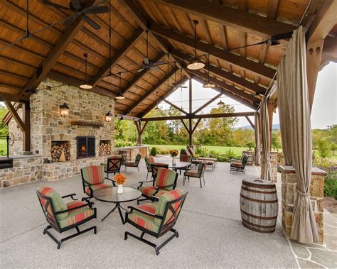 a covered patio with chairs and tables next to a fire place in front of a stone fireplace