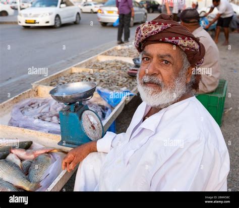 Elderly Omani fishmonger showing a fish at roadside fish market in Muscat, Sultanate of Oman ...