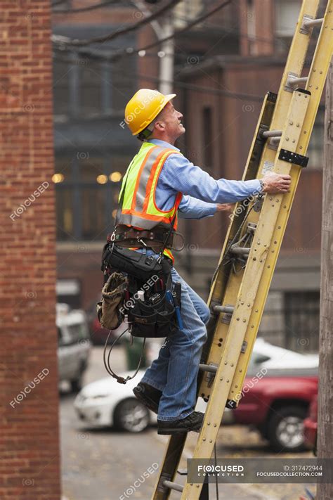 Cable lineman climbing up a ladder on city building — Tool Belt, on the ...