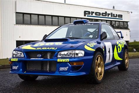 a blue subaru racing car parked in front of a building with a logo on it