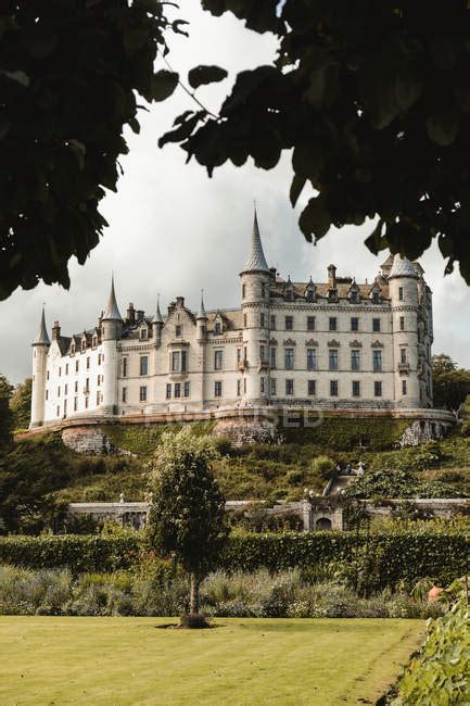 Scenic landscape of beautiful medieval Scottish castle with garden on green hills against cloudy ...