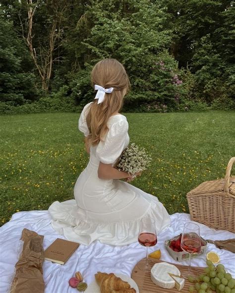 a woman sitting at a picnic table with food and wine in front of her,