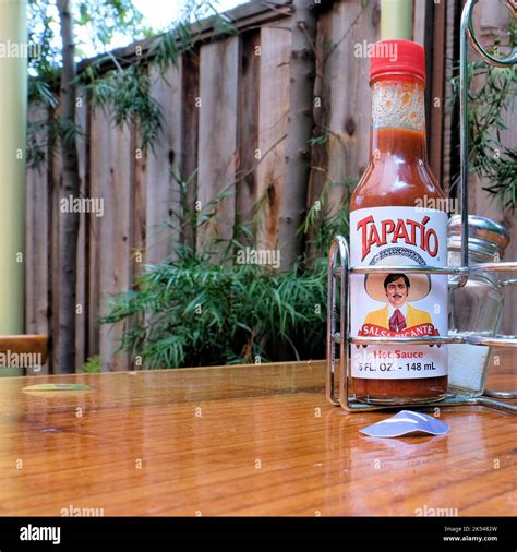 Tapatio hot sauce bottle and salt shaker in a metal condiment caddy on a wooden table in an ...