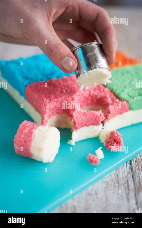 Using small round cutter to cut pieces from block of coconut mixture, making coconut bites Stock ...