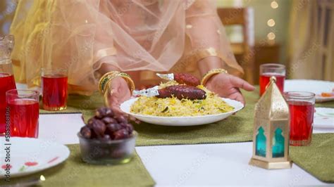 Close up shot of muslim woman hands placing chicken biryani plate on dining table at home ...