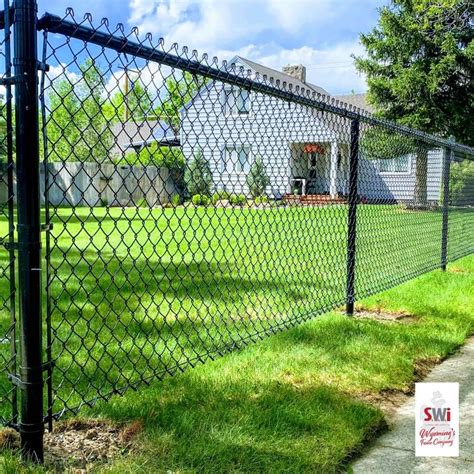 a black chain link fence in front of a house with grass and trees behind it