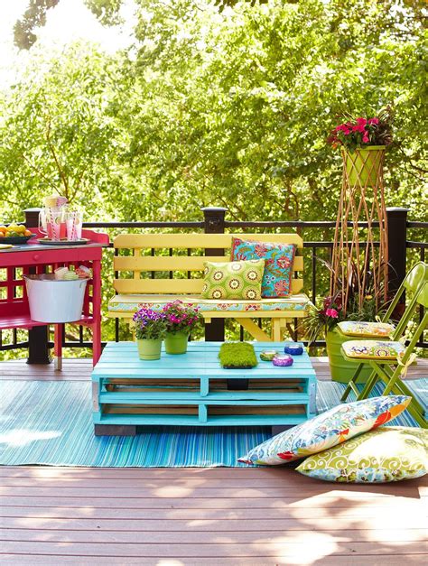 an outdoor deck with colorful furniture and potted plants on the table, in front of trees