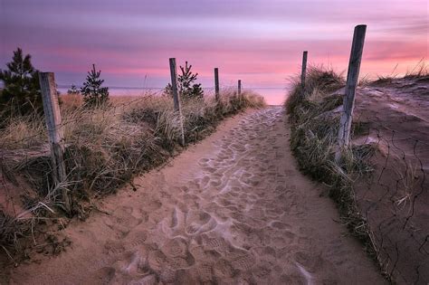 the path to the beach is lined with grass and fence posts, leading into ...