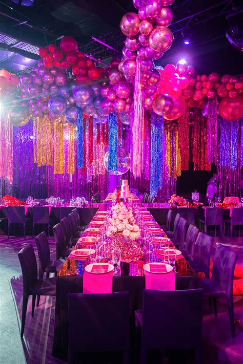a long table set up with purple and pink decorations, balloons and streamers on the ceiling