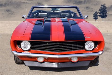 an orange and black striped car parked in a parking lot with mountains ...