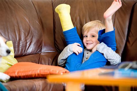 Cute little blond boy with broken leg in cast sitting on leather couch ...