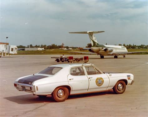 an old police car parked in front of an airplane