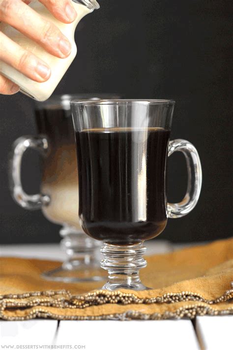 someone is pouring something into a glass cup with liquid in it and another mug behind them