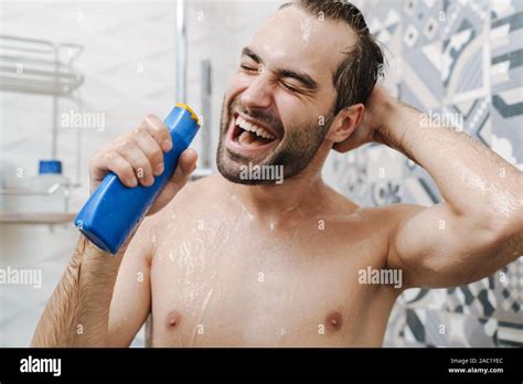 Attractive young cheerful man singing while washing in the shower ...