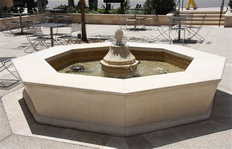 an outdoor fountain in the middle of a plaza with tables and chairs around it,