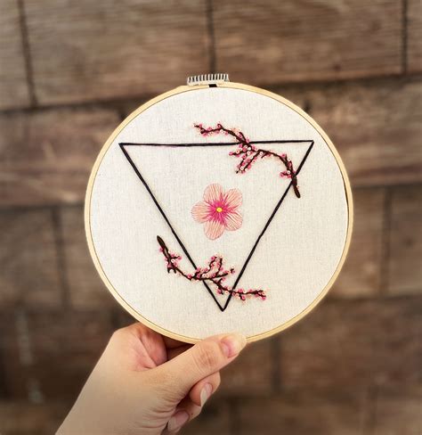 someone is holding up a embroidery project with pink flowers on the bottom and triangle in the ...