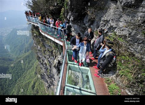 Tourists walk on the glass skywalk on the cliff of Tianmen Mountain (or Tianmenshan Mountain) in ...