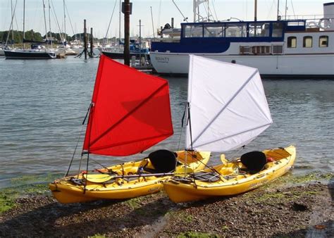 two yellow kayaks with red sails are on the shore next to a white boat