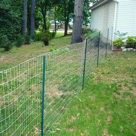 a fence that is next to a house in the grass with trees around it and a building behind it