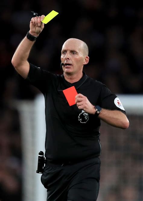 the referee is holding his yellow card in one hand and pointing to it with both hands