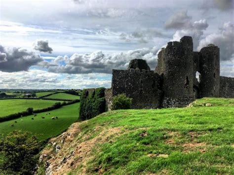 an old castle sitting on top of a lush green hillside under a cloudy ...