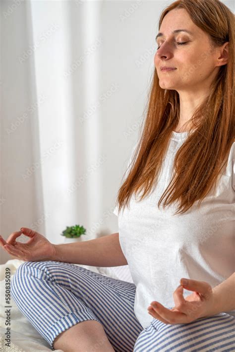 Woman doing exercises in bed at home in the morning. Sukhasana yoga pose open mind. Lady with ...