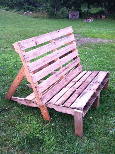 a wooden bench made out of pallets in the grass with trees in the background