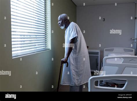 African american male patient with cane looking through the window in hospital patient room ...