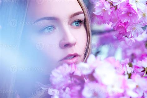 Gorgeous young blond with blue eyes looking away in blooming pink ...