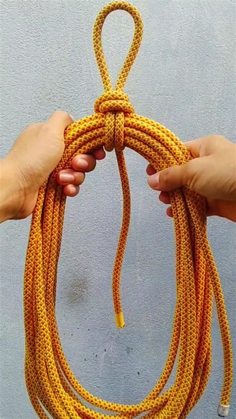 two hands holding a yellow rope in front of a gray wall