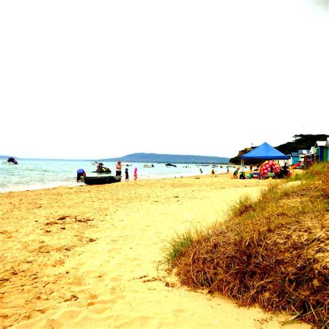 people are on the beach with boats and umbrellas in the water near some grass