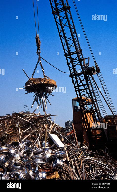 A giant crane-mounted electromagnet is used to move a pile of iron and steel items at a scrap ...