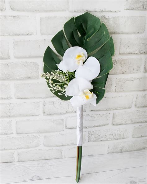 a bouquet of white orchids and greenery on a wooden table next to a brick wall