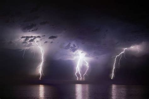 Time-lapse photo of three bolts of lightning striking the ocean from storm clouds at night ...