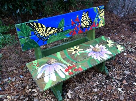 a painted wooden bench sitting in the middle of some leaves and grass with two butterflies on it