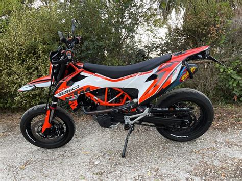 an orange and white dirt bike parked on top of a gravel road next to trees