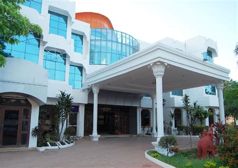 a large white building with blue windows and columns on the front, surrounded by greenery