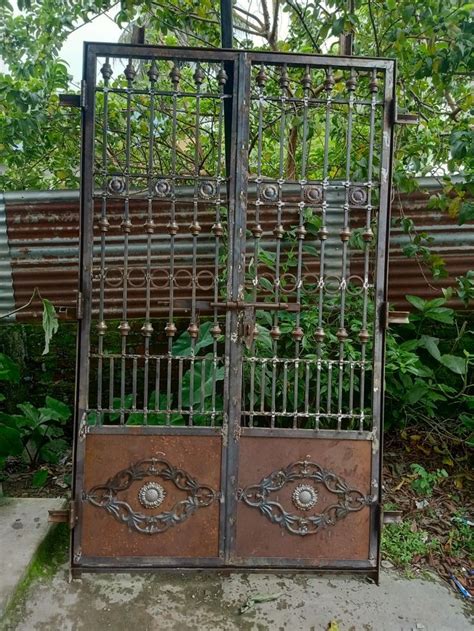 an iron gate is open in front of a wooden bench and some plants on the ground