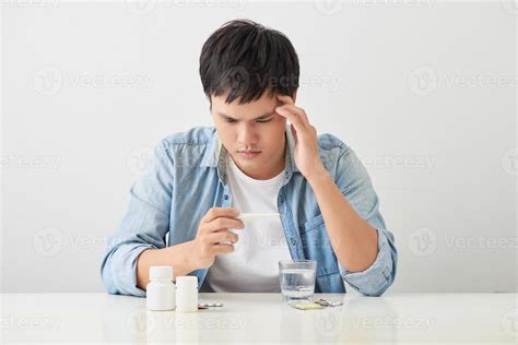 Sick young man looks at a thermometer 12746098 Stock Photo at Vecteezy