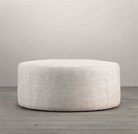 a white round ottoman sitting on top of a wooden floor next to a gray wall