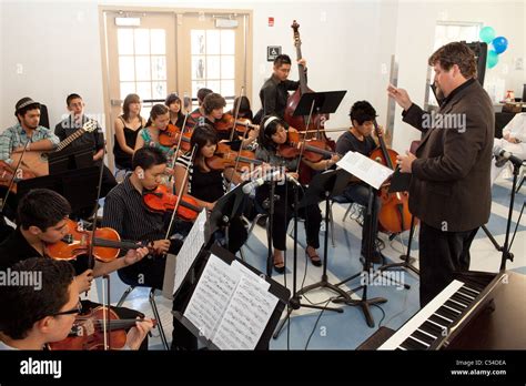 Students play stringed instruments, teacher conducts in orchestra class at Mission Early College ...