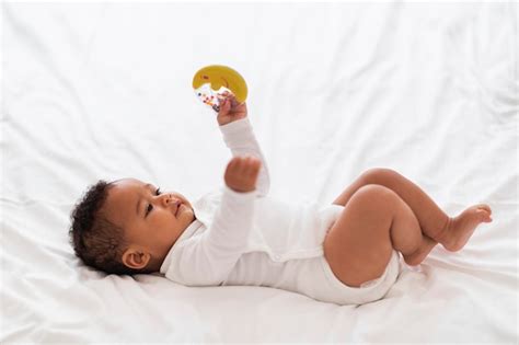 Premium Photo | Cute Small Black Baby With Rattle Toy In Hand Relaxing In Bed