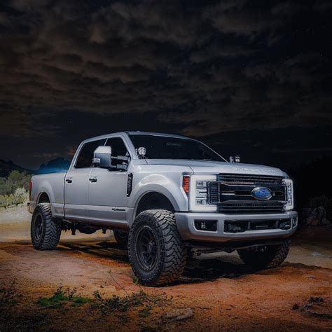 a white truck parked on top of a dirt field at night with clouds in the ...