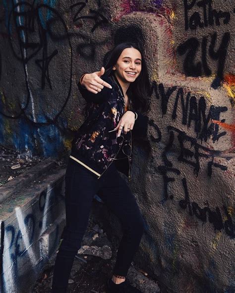 a woman standing next to a wall with graffiti on it and pointing at the ...